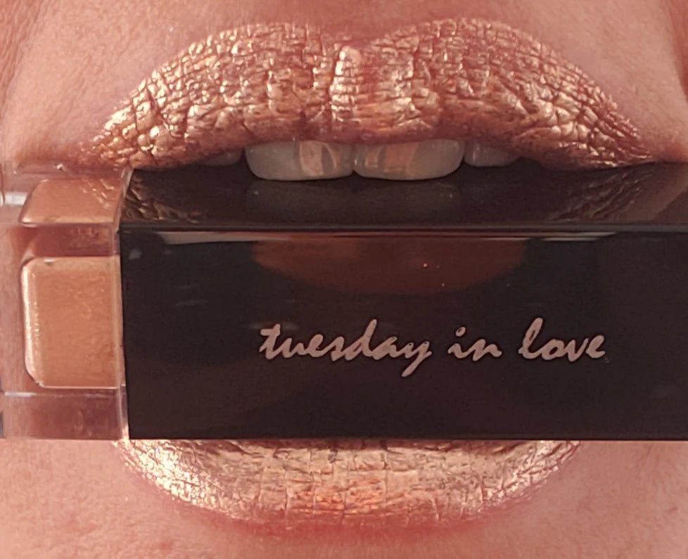 Vrouw die speels een flesje Hunny TUESDAY IN LOVE Lipstick tussen haar tanden houdt